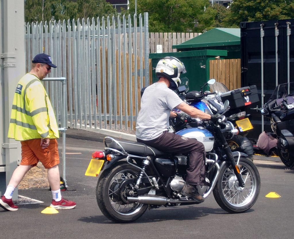 A instructor in hi-vis vest explaining to a motorcycle rider how they should practise riding slowly through a turn